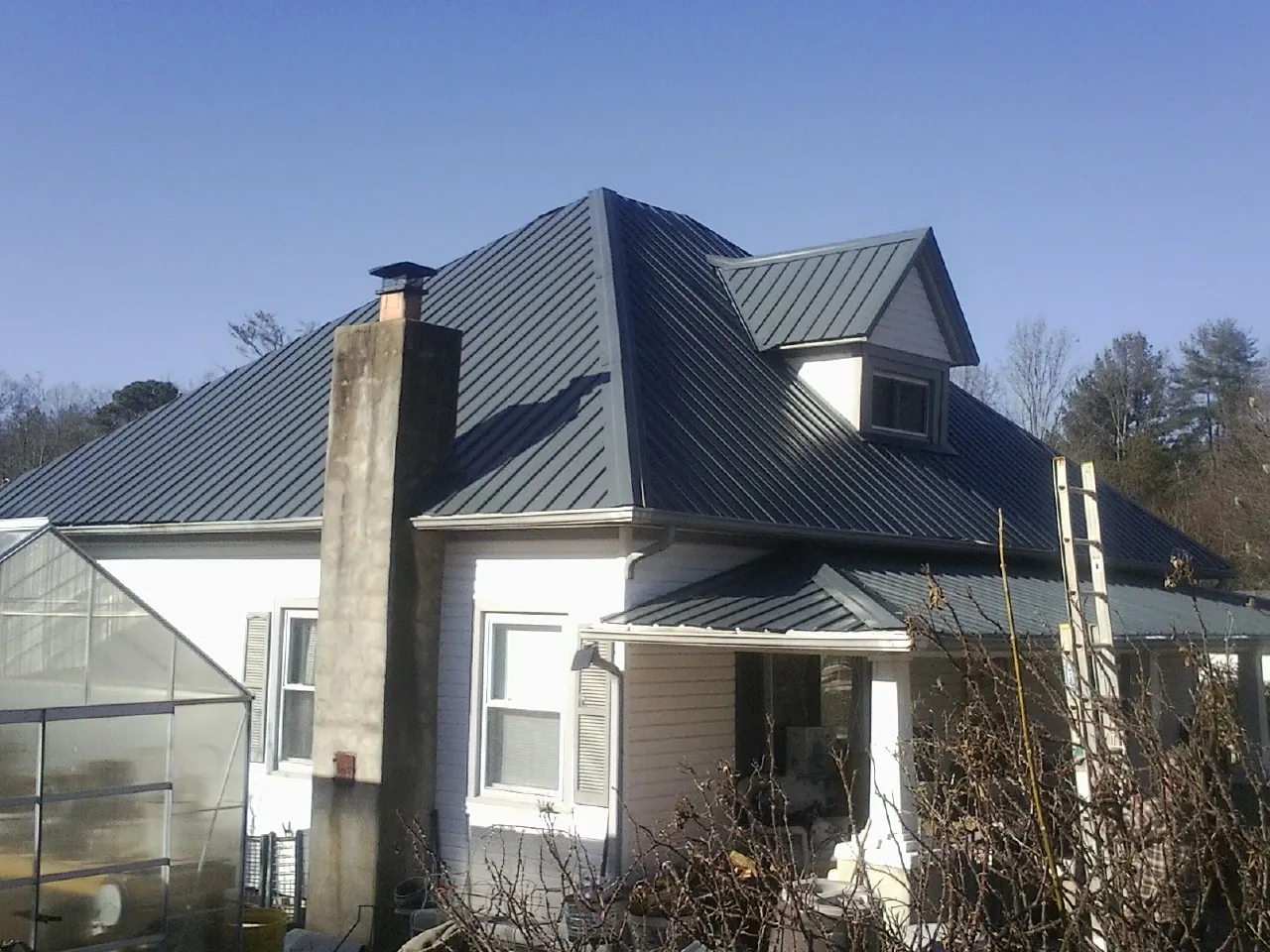 Dark blue standing seam metal roof on a white farmhouse with dormer — Slate & Tile Roof Repair by Roofing Brothers in Cherry Plain
