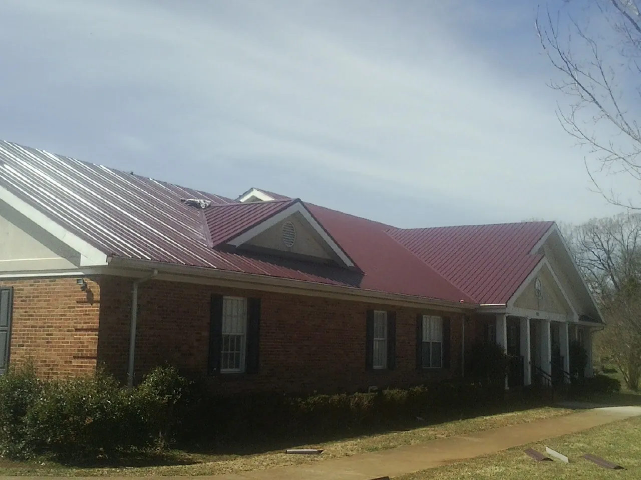 Red metal roof with gabled entries on a long brick building, from a Hail Damage Roof Repair job in Cherry Plain