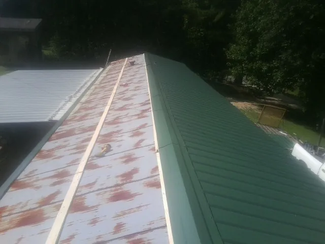 Old rusted panels beside newly installed green metal roofing — Wind Damage Roof Repair by Roofing Brothers in Cherry Plain