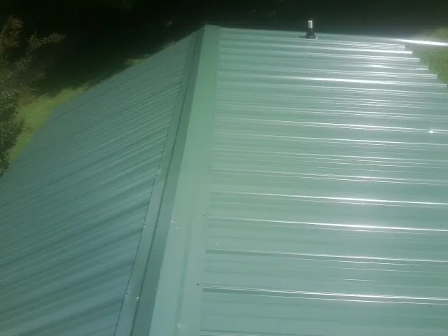 New green metal panels meeting at the ridge of a roof — Flat Roof Repair work by our crew in Cherry Plain