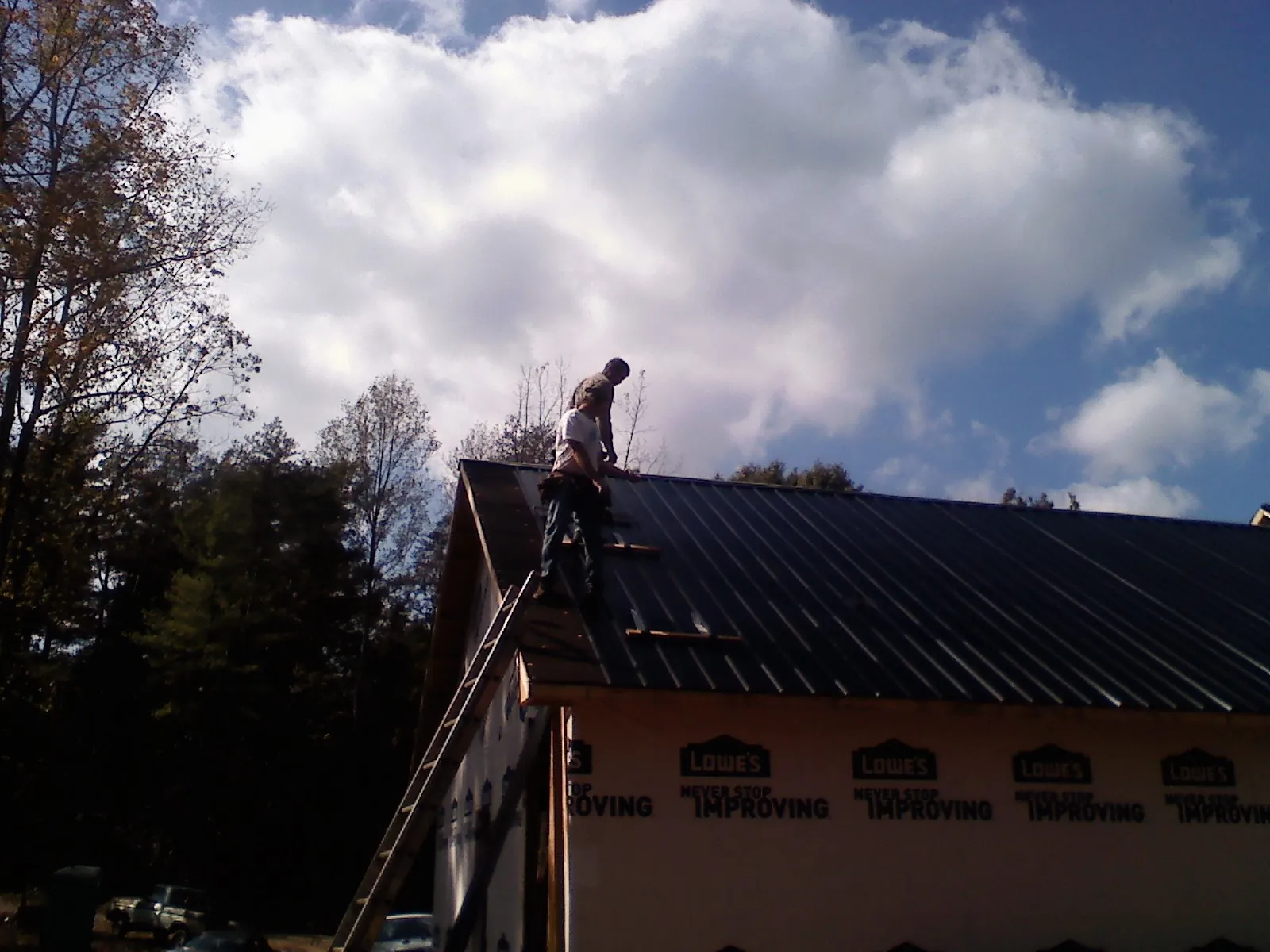 Roofer fastening dark metal panels high against a cloudy sky, from a Roof Inspection job in Cherry Plain