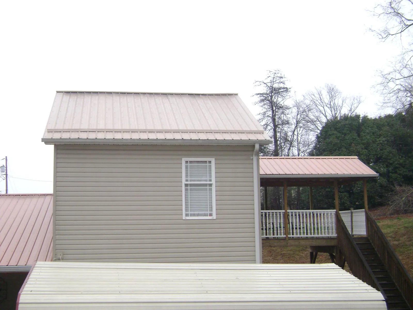 Tan metal roofs on a two story addition and attached porch, from a Roof Replacement job in Cherry Plain