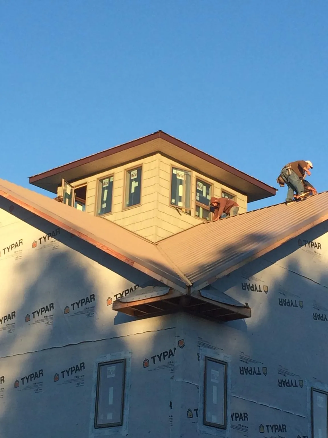 Roofers working around a rooftop cupola on a new metal roof at sunset — Roof Waterproofing in Cherry Plain by Roofing Brothers